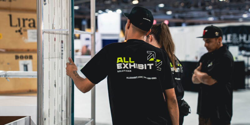 Team member from All Exhibit Solutions setting up a trade show booth panel during installation.