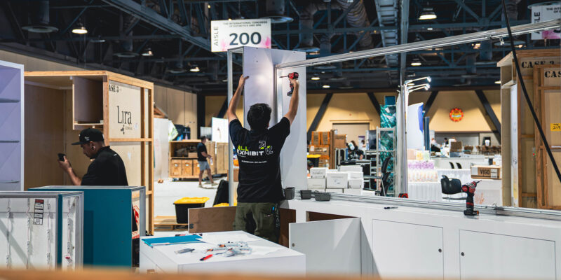 Crew member preparing booth framework among shipping crates.