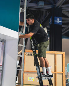Installer on ladder securing booth panel for trade show setup.
