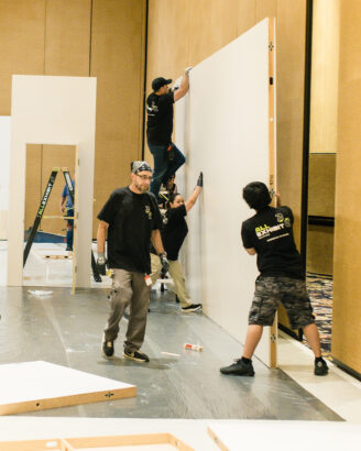 All Exhibit Solutions team installing a large wall panel during trade show booth setup.
