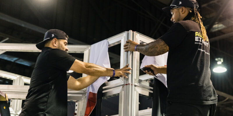 Two installers aligning and fastening booth frame panels.