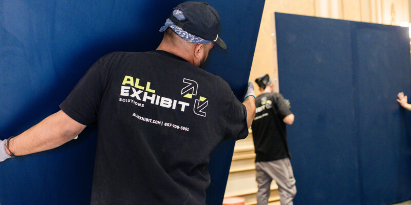 All Exhibit Solutions team lifting and positioning a large blue wall panel.
