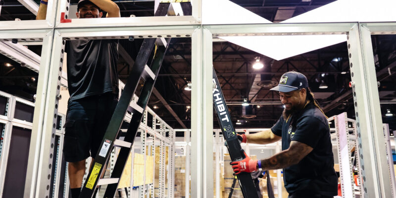 Team aligning structural frame beams for booth assembly.