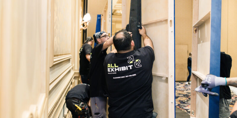 Crew members installing booth wall panels at a trade show venue.