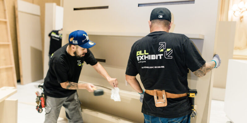 Team assembling display shelving unit during booth construction.