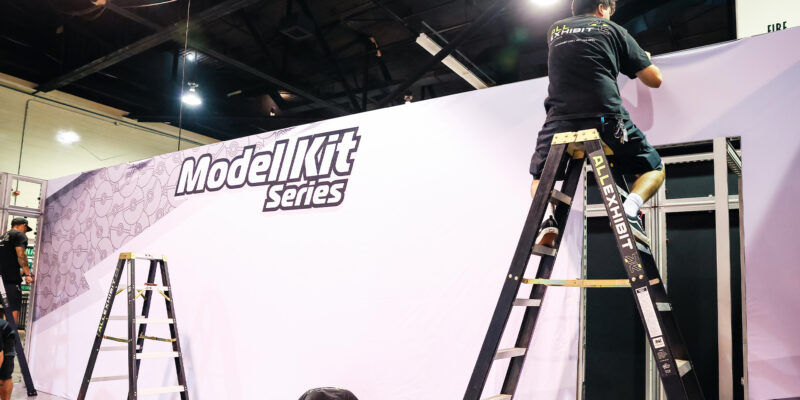 Worker on ladder attaching panel to branded trade show wall.