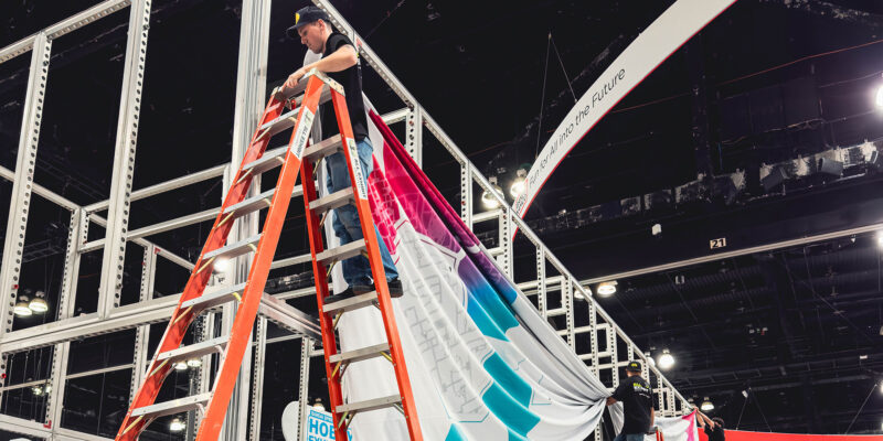 Crew member on ladder working on overhead booth truss system.