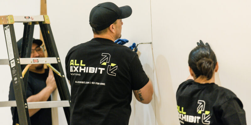 Installers securing large wall panels for a trade show booth setup.