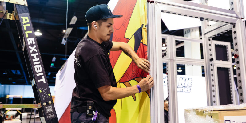 Installer adjusting colorful booth panel with branding graphics.