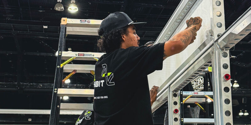 Installer securing white frame beams during booth construction.