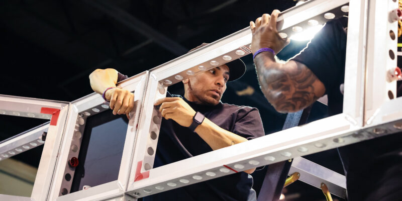 Team members securing booth frame structure during setup.