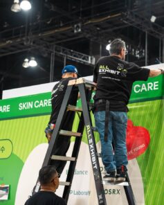 All Exhibit Solutions crew installing the green Seongsu skincare graphic wall at the Olive Young FESTA booth, KCON LA 2026