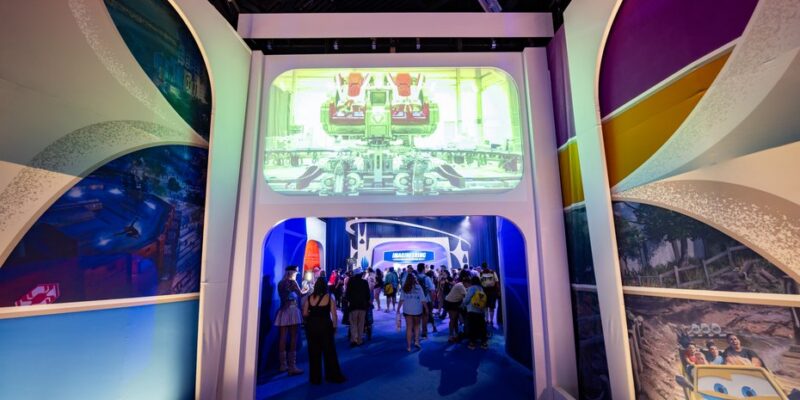 Scenic portal into a themed zone of the Walt Disney Imagineering pavilion at D23 2026, with an attraction render on the overhead screen