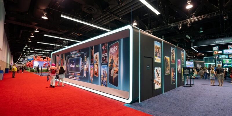 Walk-through poster gallery lined with backlit title panels inside the Disney+ and Hulu pavilion